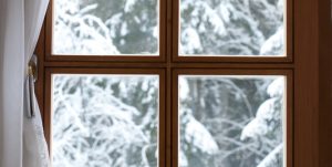A close-up image of a window with a wood grid pattern looking out over snow covered trees.
