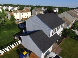 An aerial image of a white, two-story home with a new, dark-gray asphalt shingle roofing system.